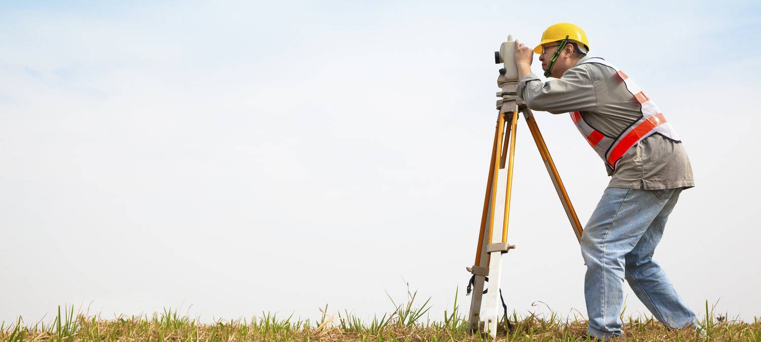 an image of a man looking thru a theodolite, it's a sunny summer day.