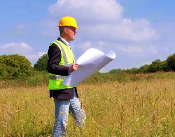 man holding land survey plans walking in a field