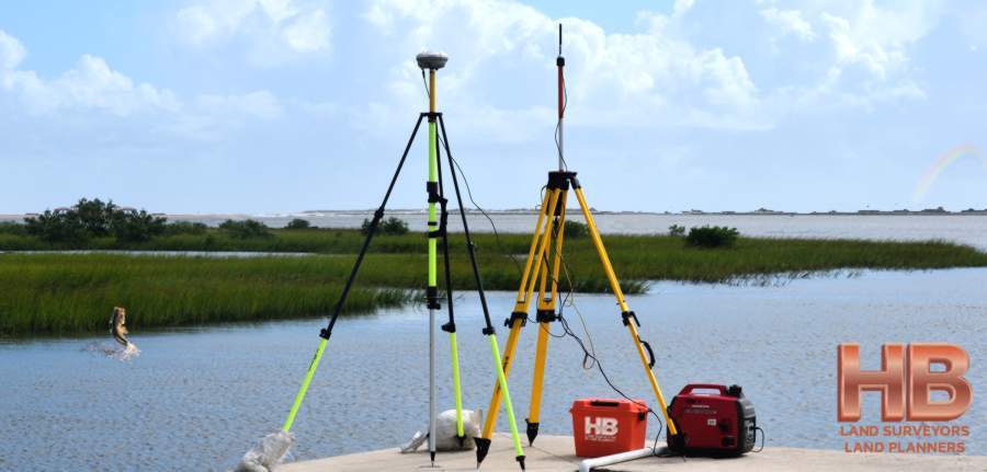 An image of 2 tripods with radio connection survey devices, the background is a beautiful lake and cat tail wet-land there is a large mouth bass jumping out of the lake and there is a very slight rainbow, it's a really cool image!