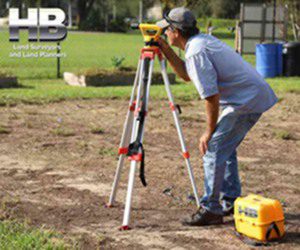 Image of a Surveyor Looking Thru a Leveling Instrument while performing a Property Survey. He is in the backyard of a house in Frederick. 