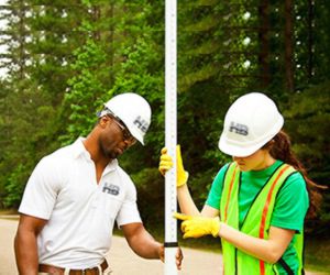 an image of a man of color and a woman of color looking at a leveling rod or prism pole. It looks to be a very sunny summer day.