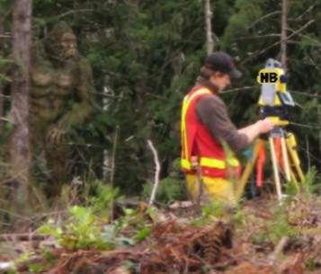 an image of a man performing a topographic survey he is in a rugged area on a hillside and bigffot is on the left blended into the trees looking at the surveyor, he he laugh out loud!!