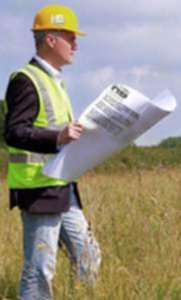An image of a man standing in tall grass holding a Boundary survey in his hands as he looks out over the property. It looks like a bright and sunny summer day. 